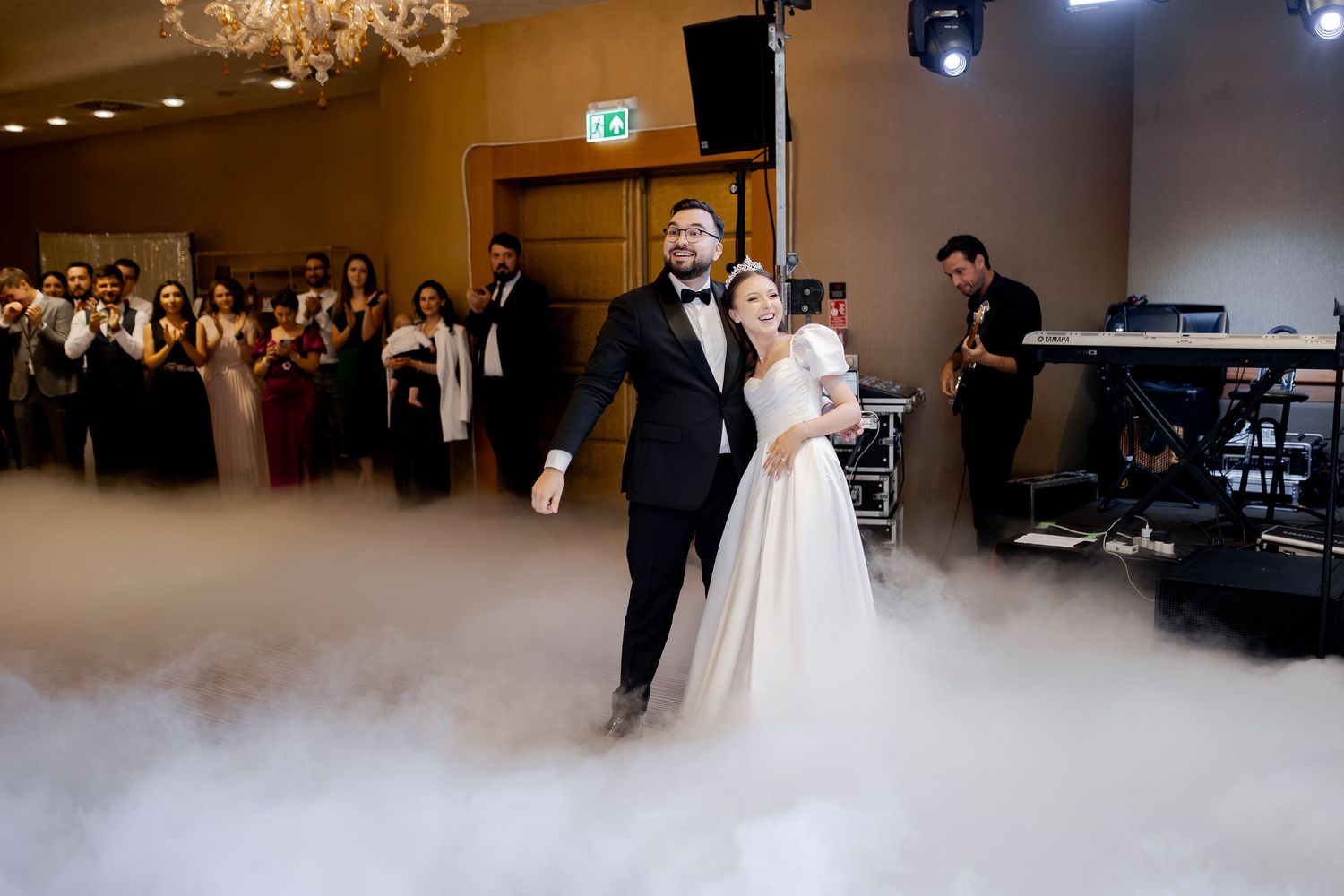 A wedding couple dances together surrounded by low-lying fog in an elegant ballroom.