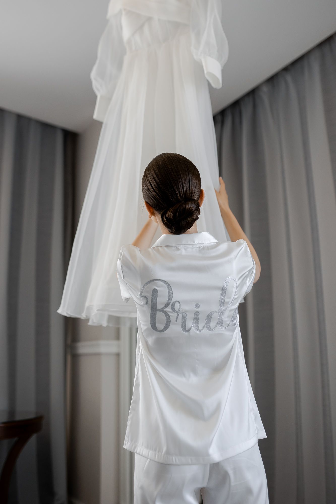 Wedding dress hanging while person in white robe reaches up to touch it.