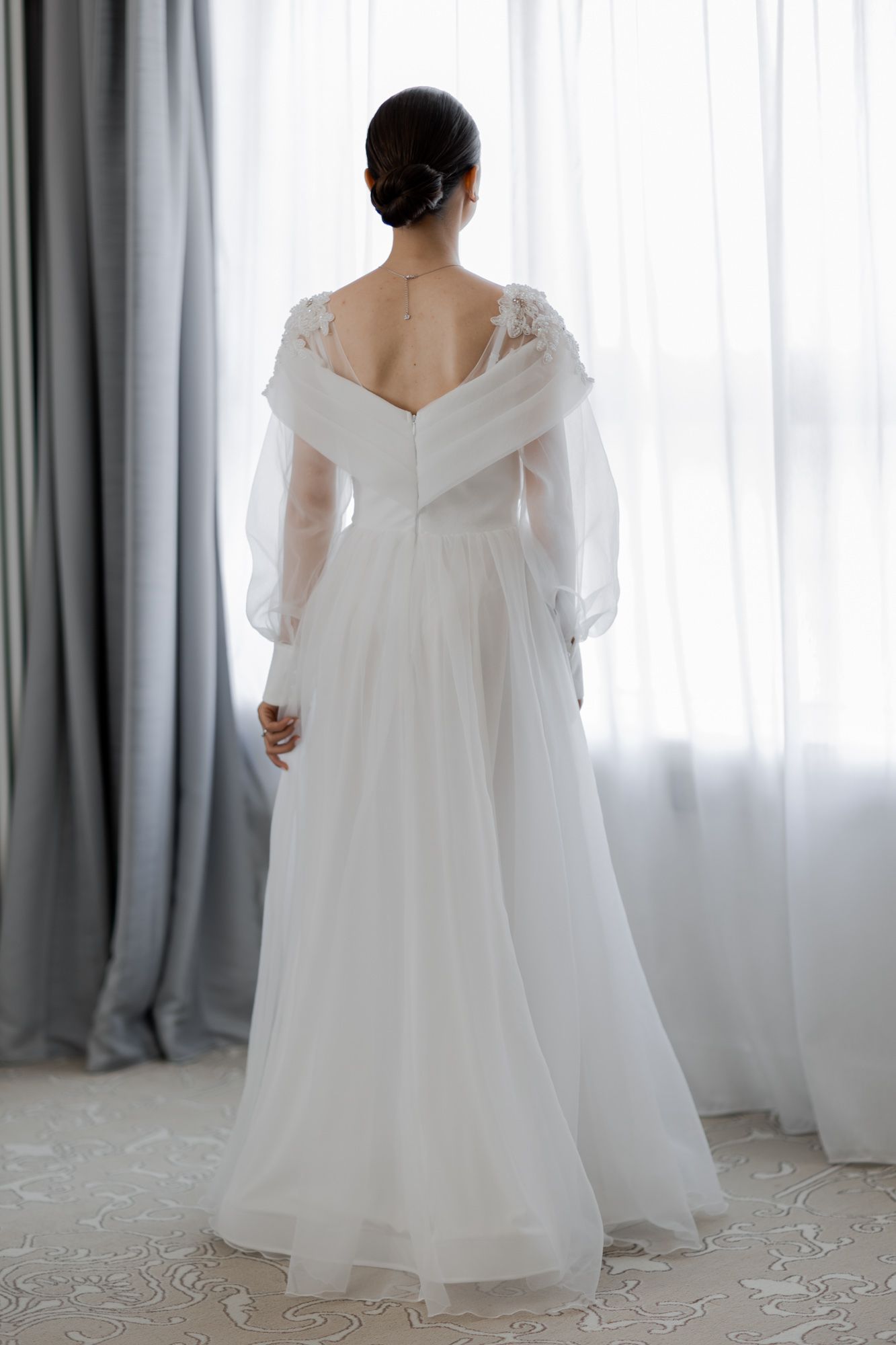 Back view of a wedding dress showing V-shaped design with lace details and long sleeves.