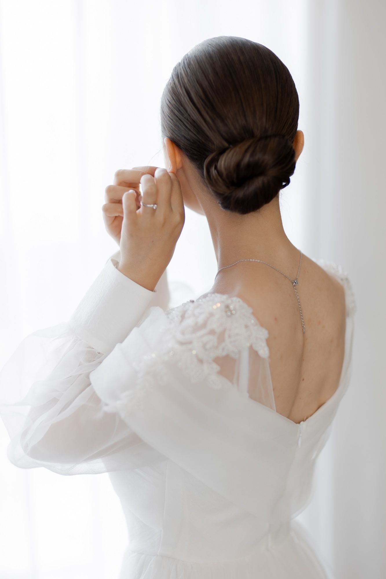 Classic bridal updo hairstyle shown from behind with wedding dress lace details.