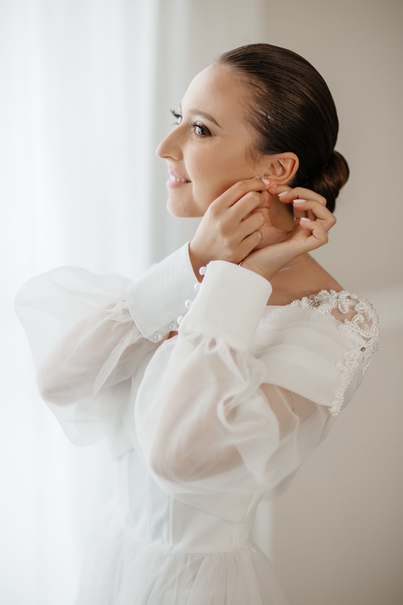 Side profile of elegant bridal look with sleek bun hairstyle and white gown.