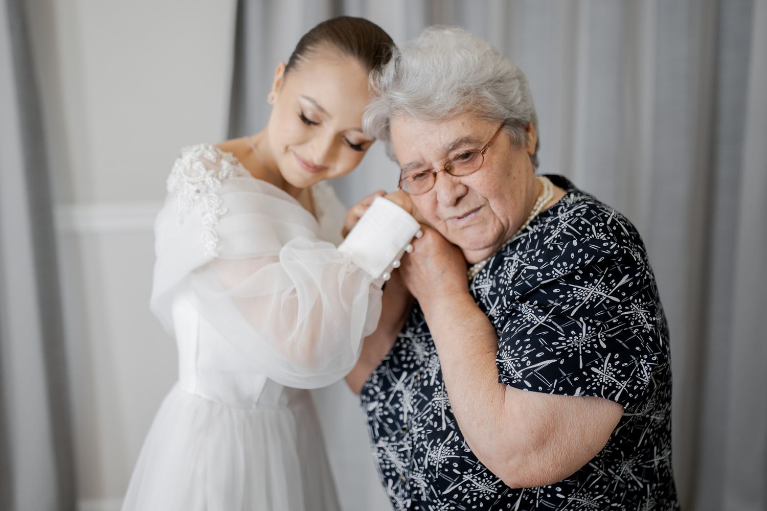 Emotional moment between bride in white gown and elderly woman in patterned black dress.