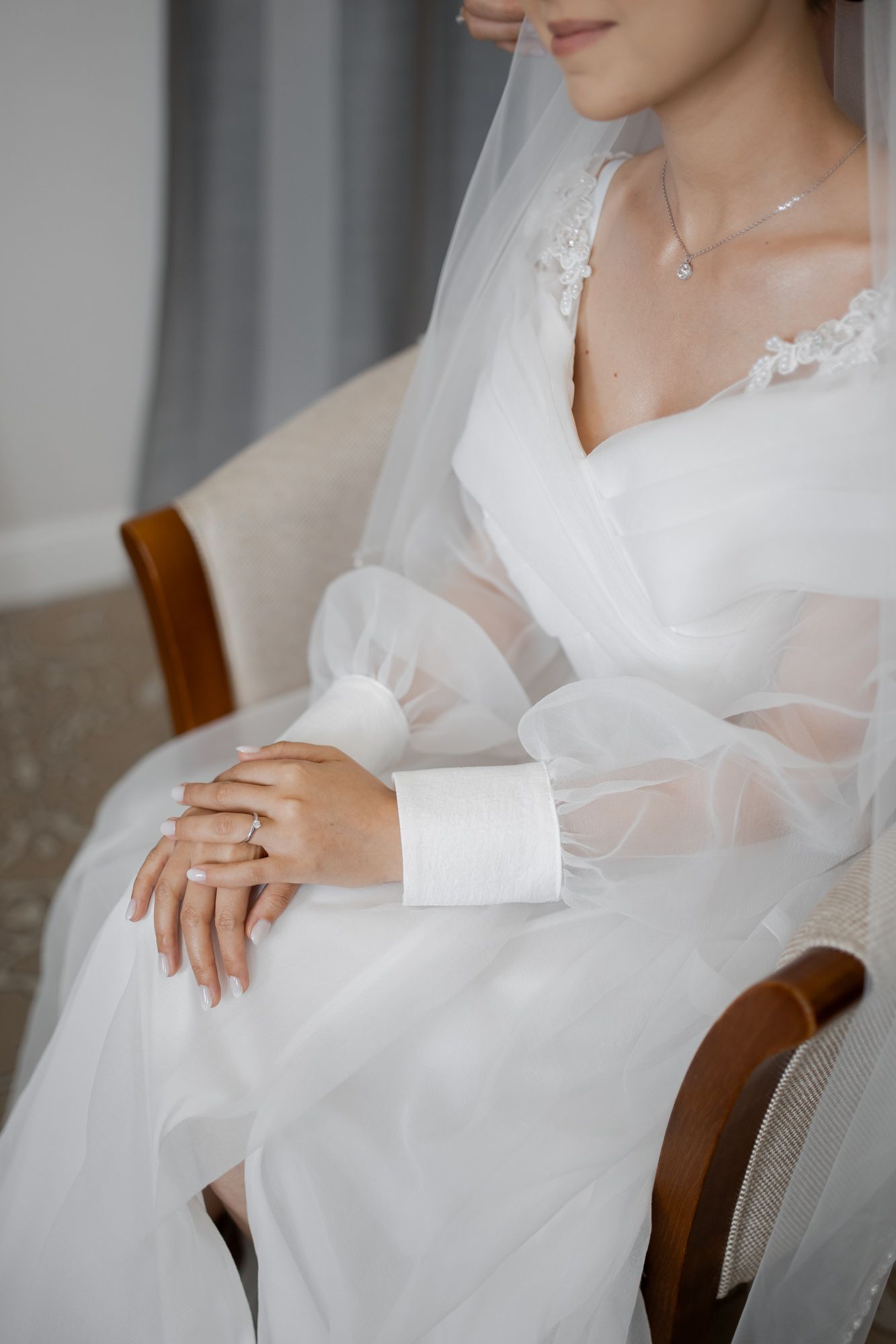 Close-up detail of bride's hands resting on white wedding dress with lace and tulle details.