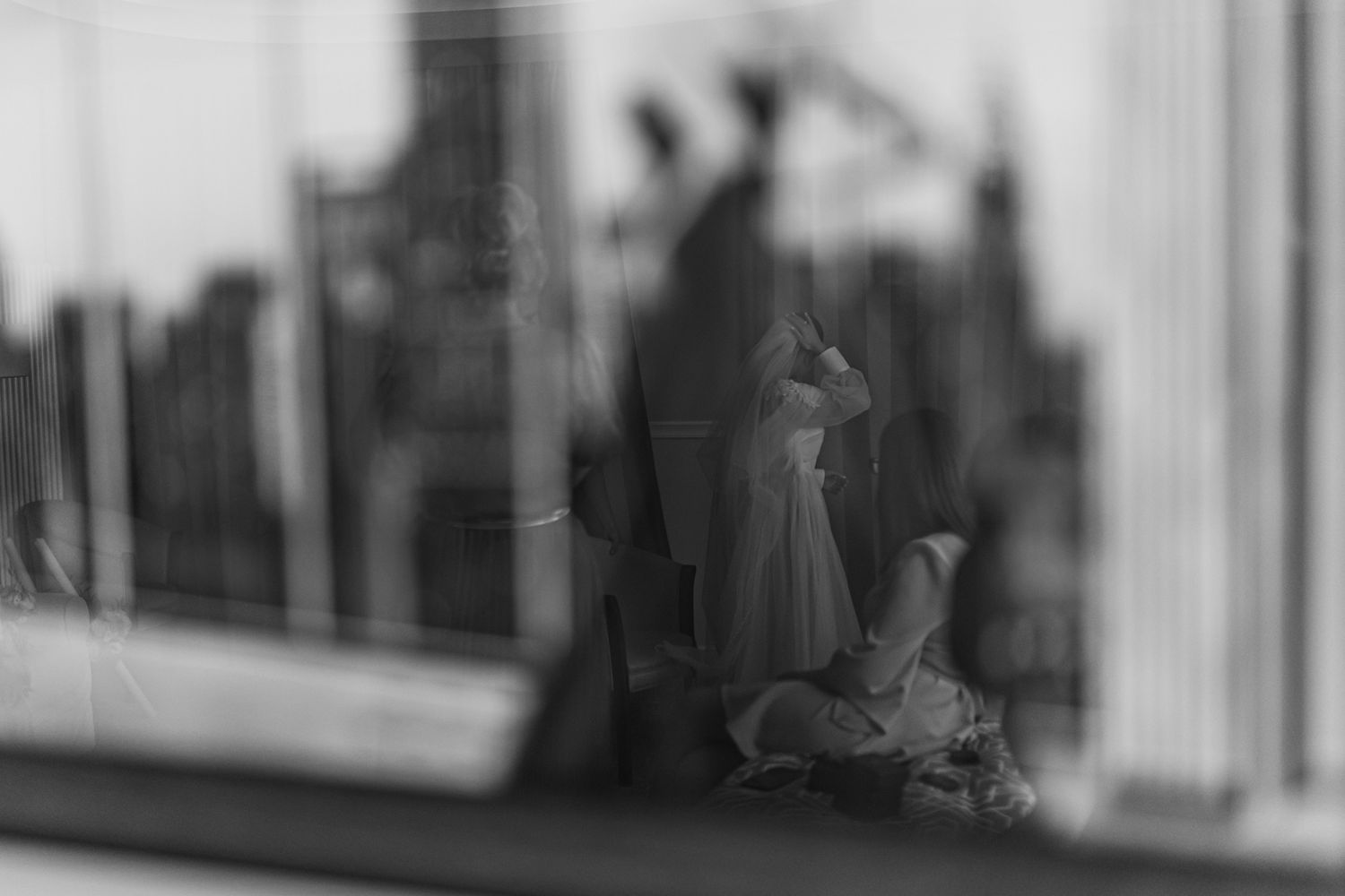 Artistic blurred black and white silhouette through window showing wedding scene.