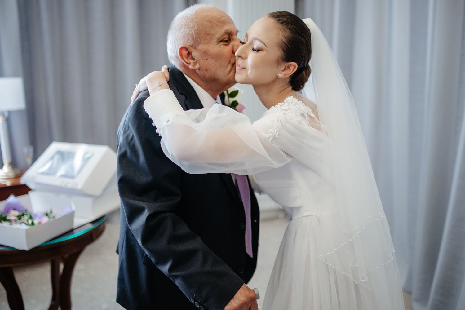 Tender embrace between bride in white wedding dress and elderly man in formal attire.