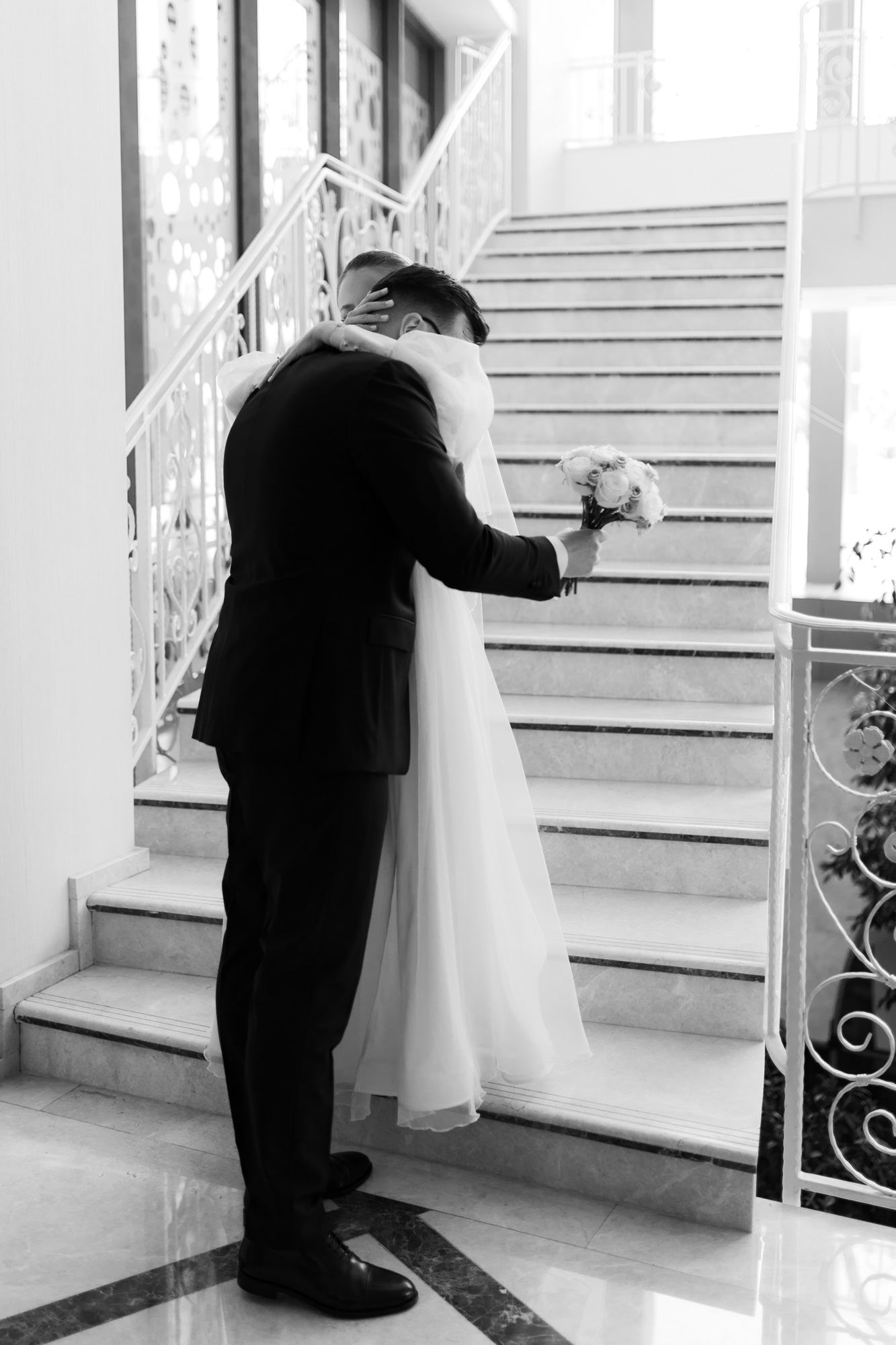 Black and white photo of couple sharing intimate moment on elegant staircase.