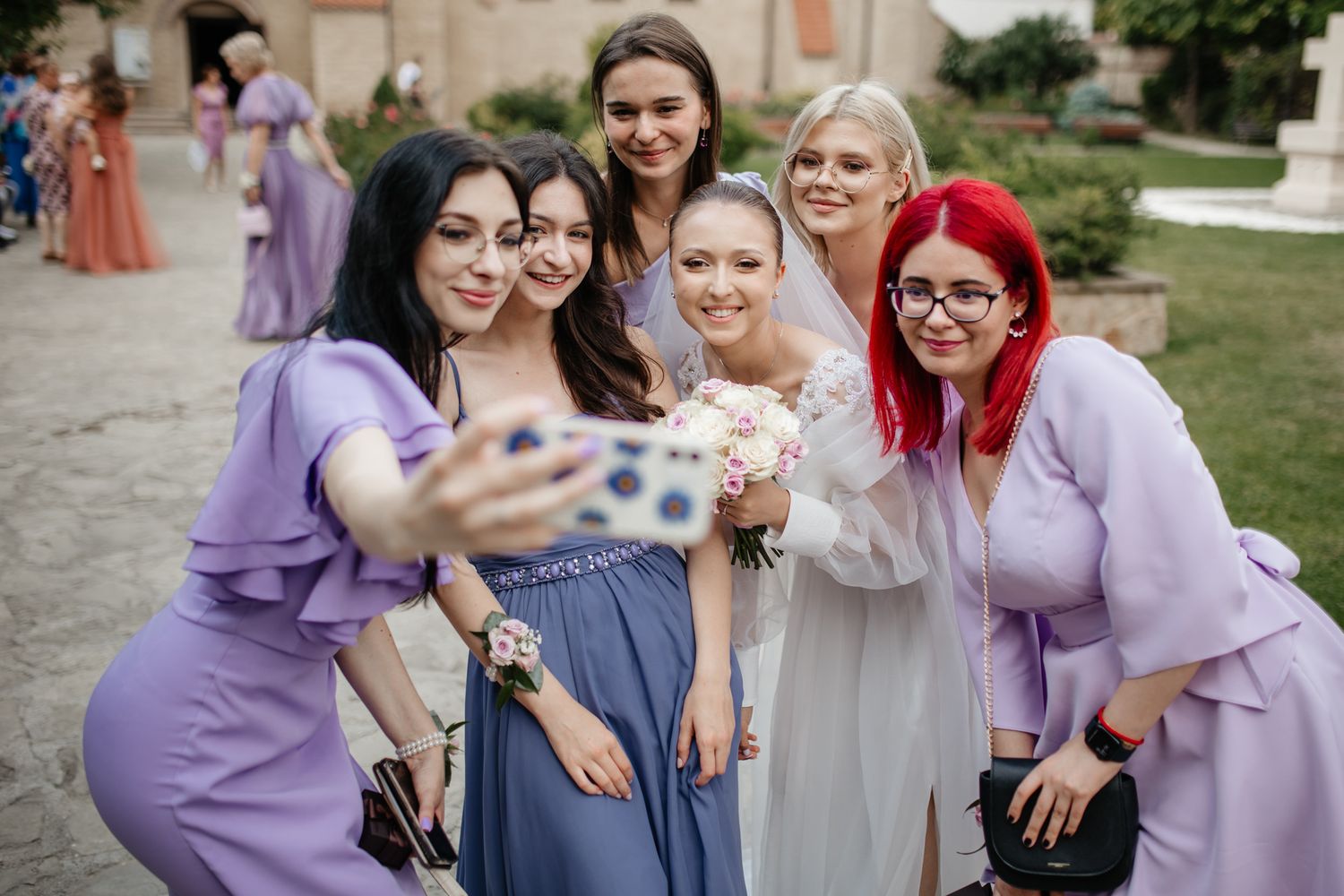 Bridesmaids in purple dresses gather for a selfie at an outdoor wedding celebration.