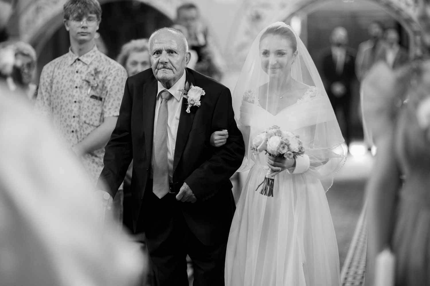 A black and white wedding ceremony photograph capturing a walk down the church aisle.