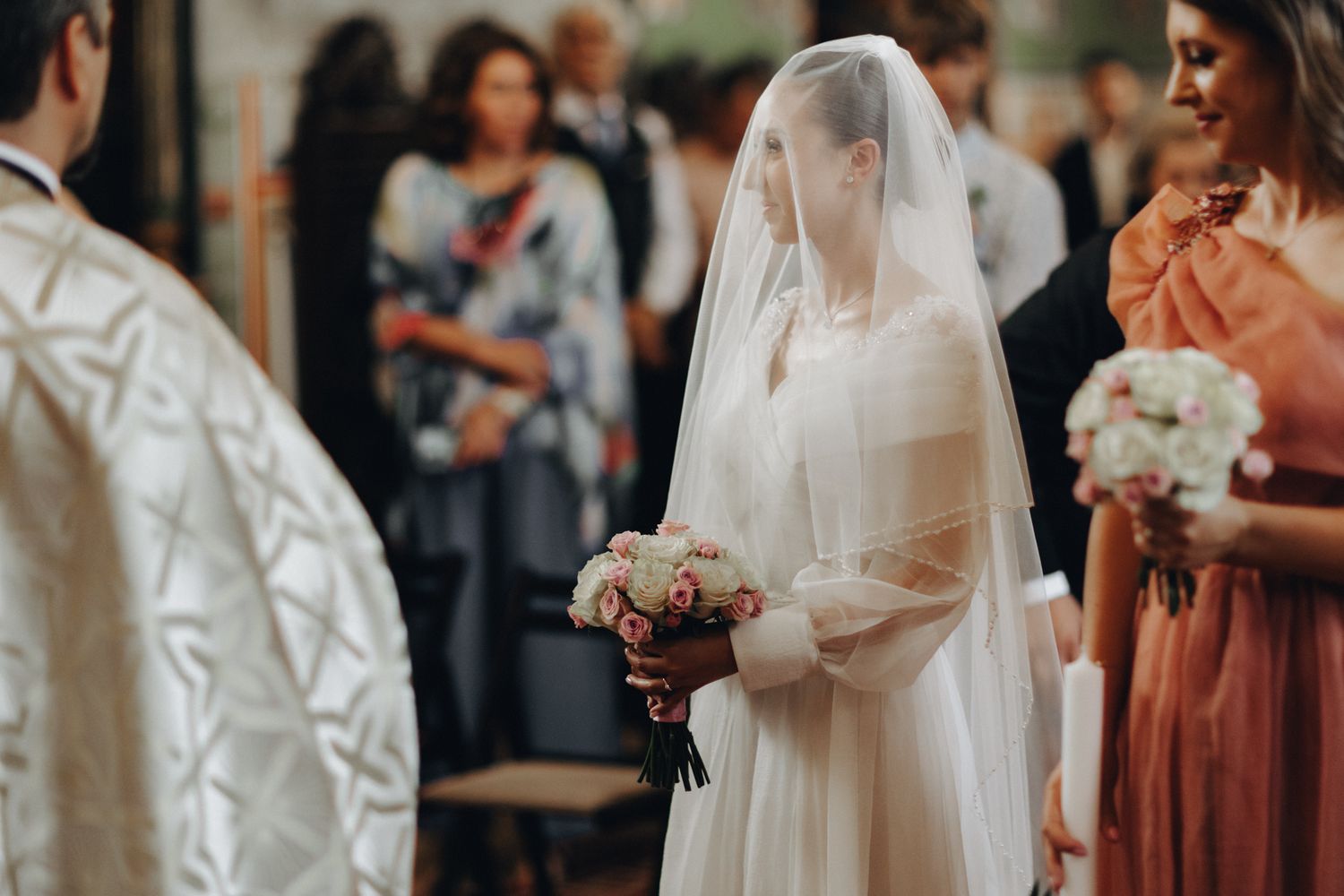 A bride in traditional white gown holds a bouquet during a sacred church ceremony.