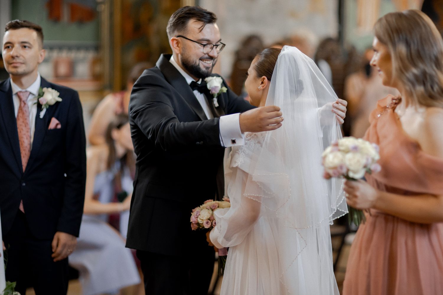 An emotional wedding ceremony moment in a church with guests watching and pink bridesmaid dresses.
