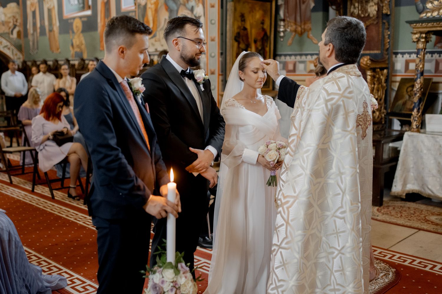 Traditional church wedding ceremony with couple and priest in white vestments holding candles.