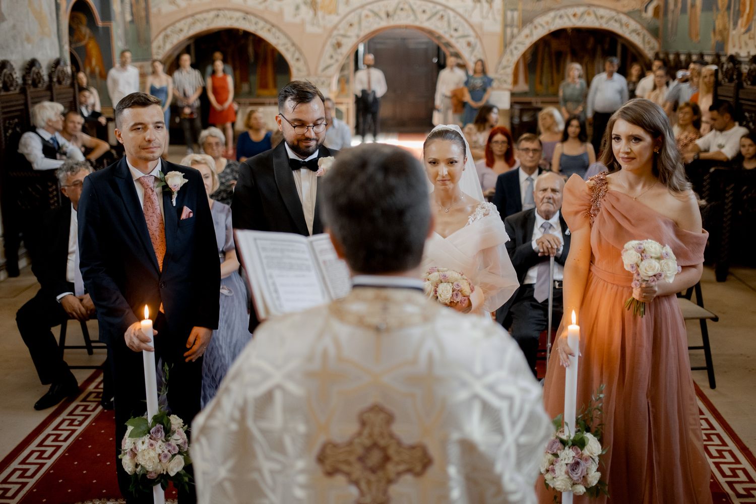 Wedding ceremony in progress inside a beautifully decorated Orthodox church with painted walls.
