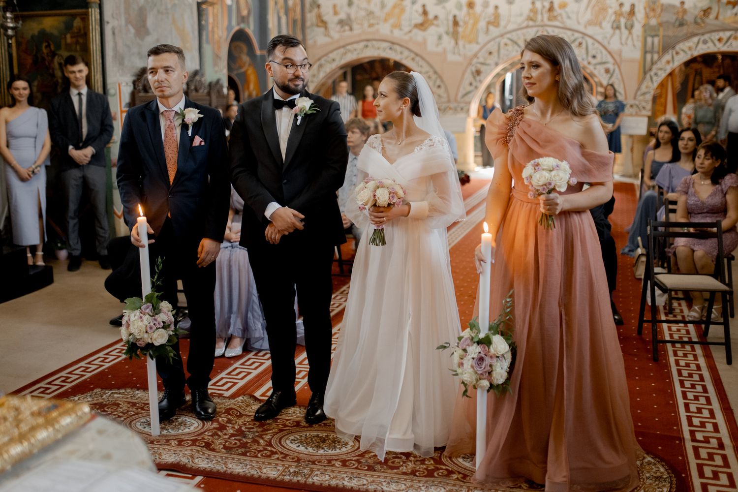 Wedding party standing at altar during Orthodox ceremony with peach-colored bridesmaid dresses.