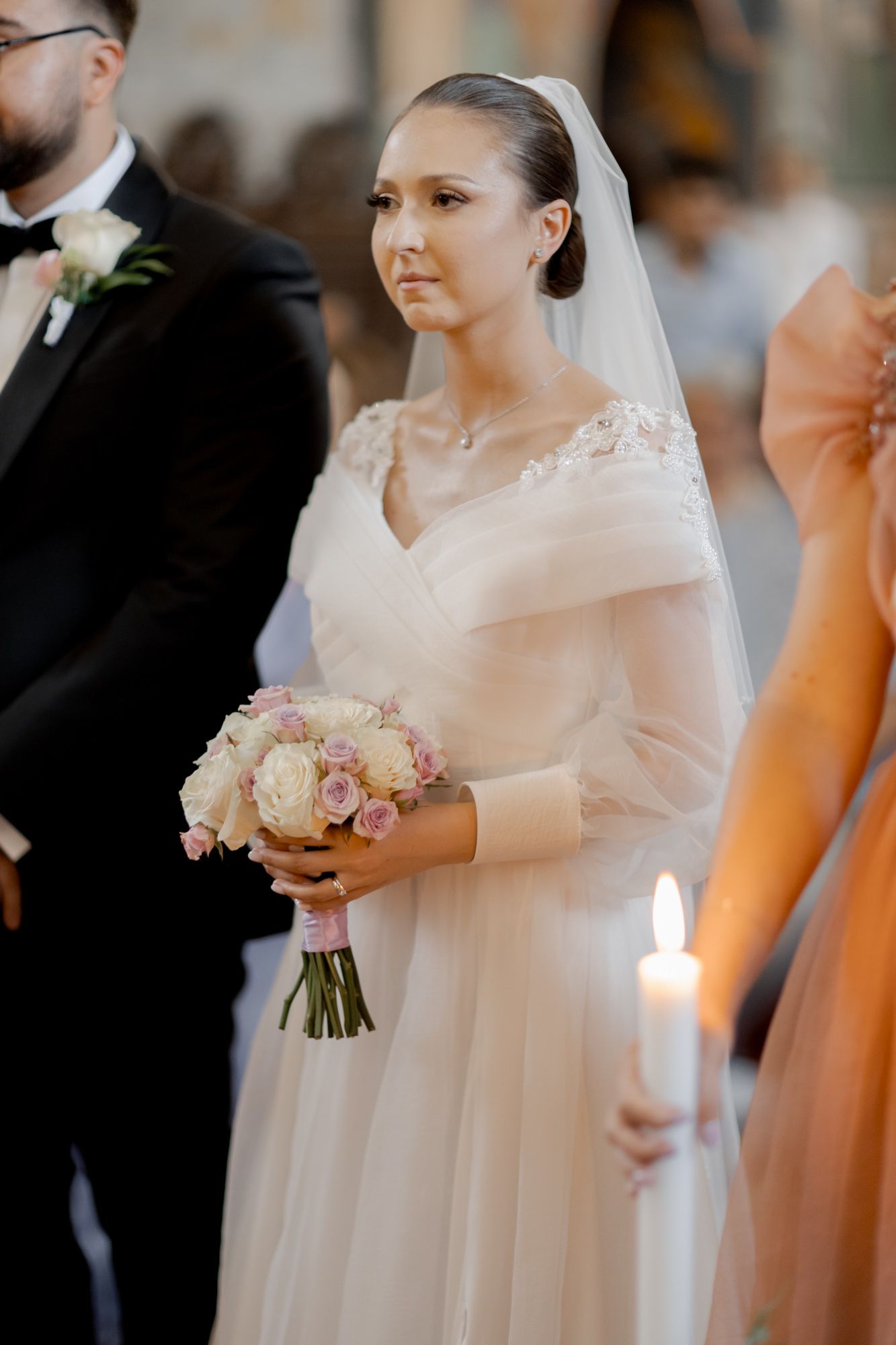Elegant bride in classic white gown holding pastel bouquet during Orthodox ceremony.