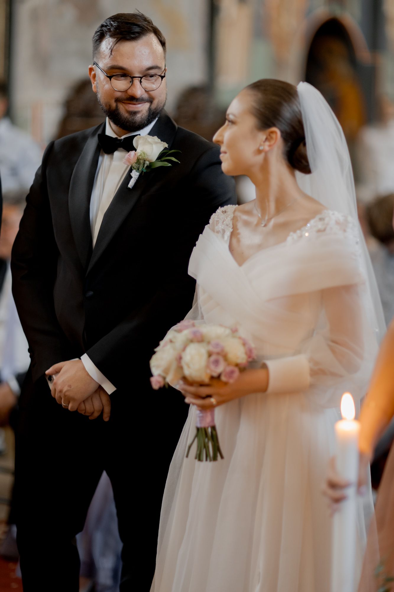 Intimate moment during Orthodox church wedding ceremony with white floral bouquet.