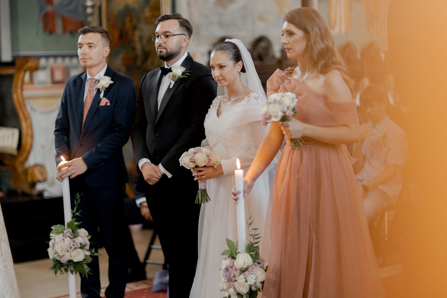 Wedding party lined up during ceremony with bridesmaids in peach dresses holding candles.