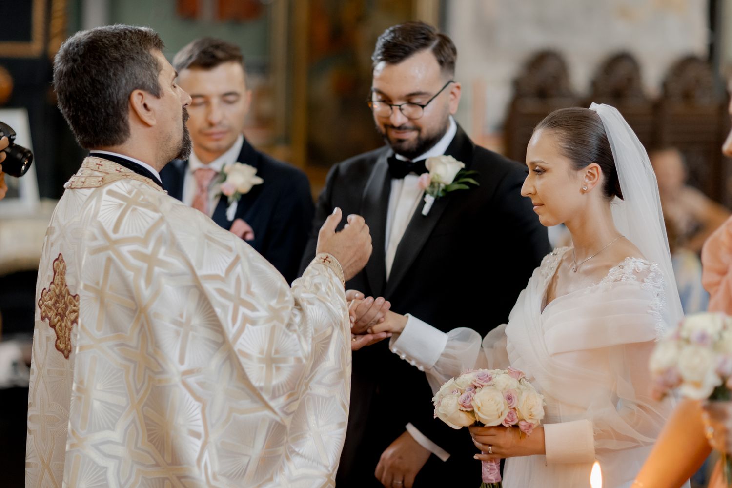 Orthodox priest performs traditional wedding ceremony in ornate church with couple exchanging vows.