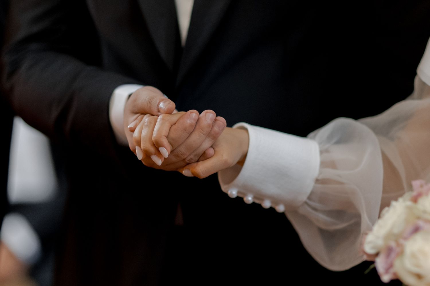 Close-up shot of bride and groom holding hands during wedding ceremony.