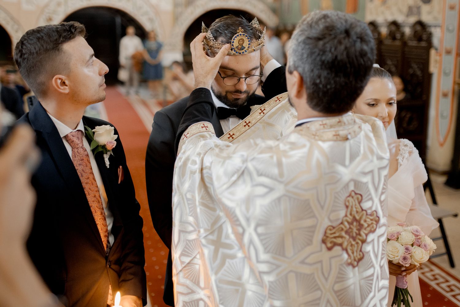 Wedding ceremony in ornate orthodox church with priest wearing traditional embroidered vestments.