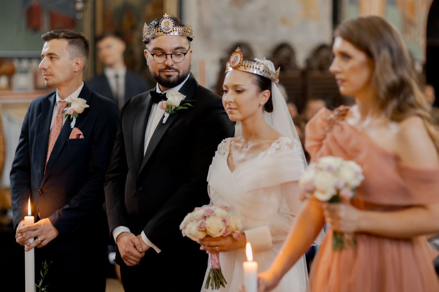 Wedding party stands at altar during orthodox ceremony with bridesmaids in coral dresses.