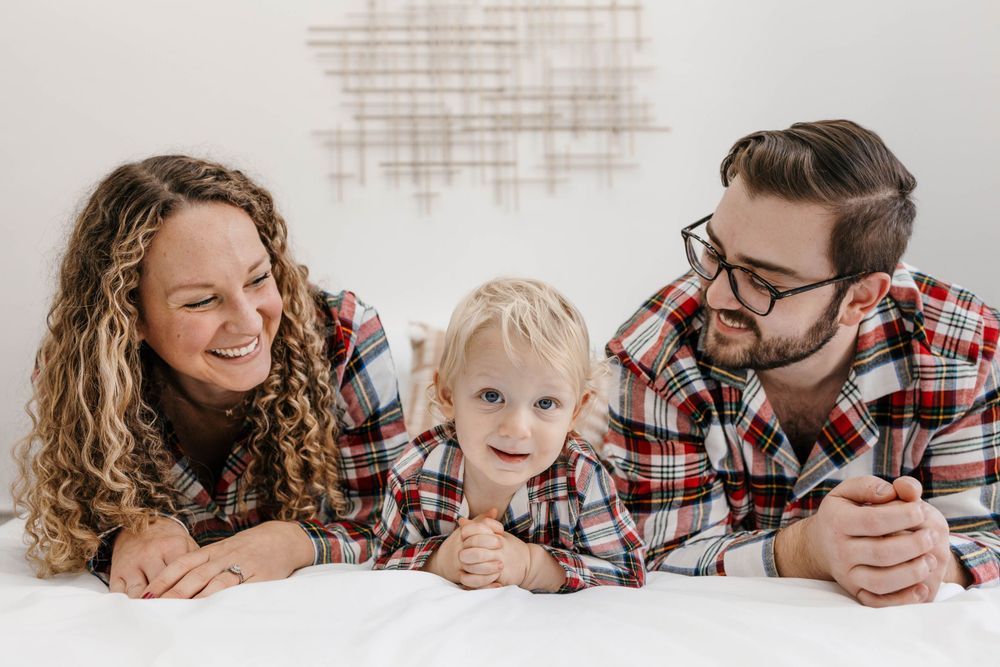 Family in Christmas pajamas laying on a bed together