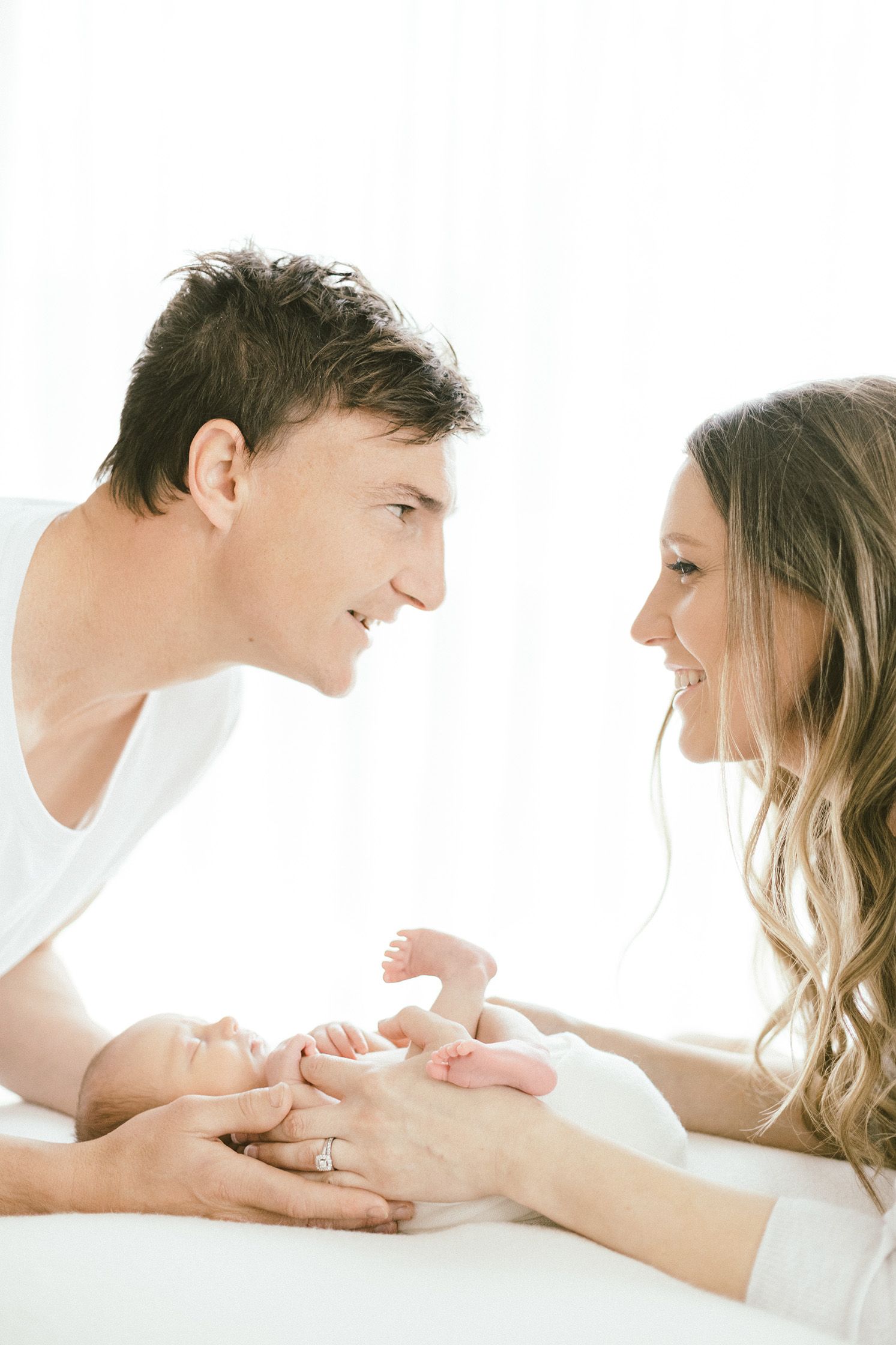 Young couple gazing lovingly at their newborn on white background.