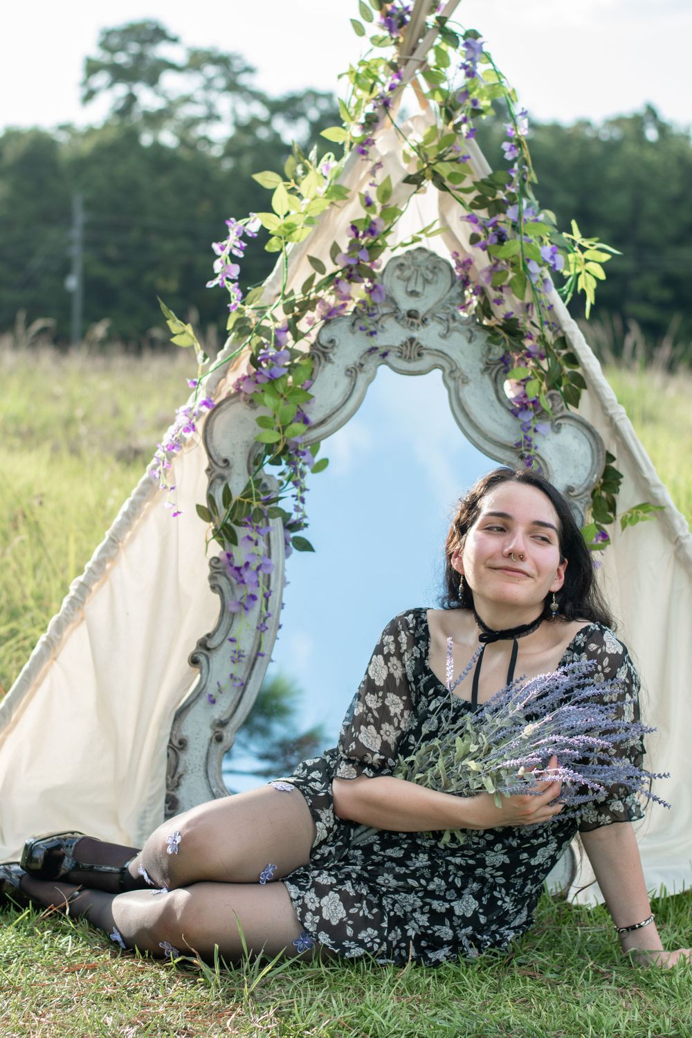 A vintage mirror display with purple flowers and white fabric forms a cozy outdoor setting.