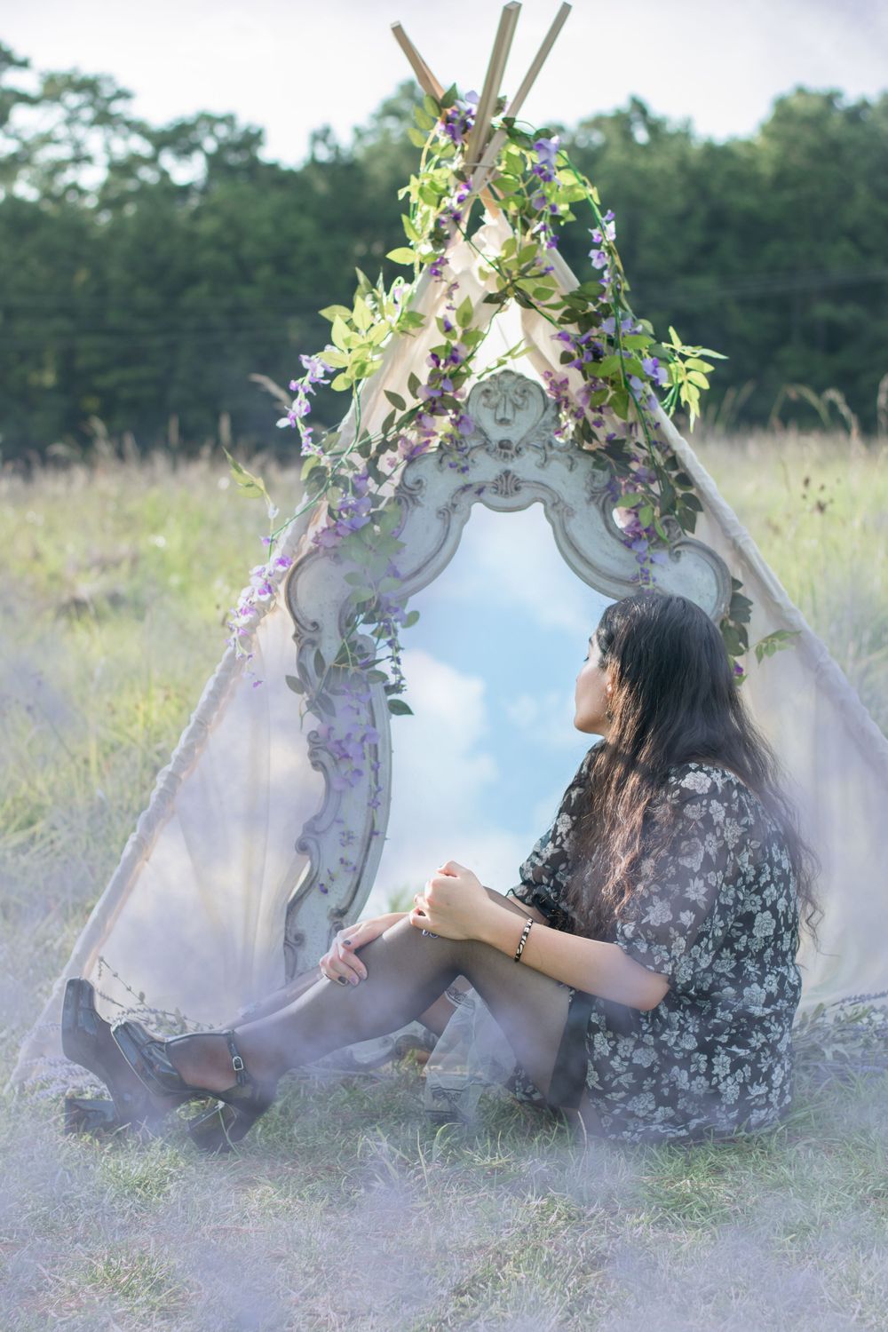 A vintage mirror set up outdoors with floral decorations and white fabric creating a tent-like structure.