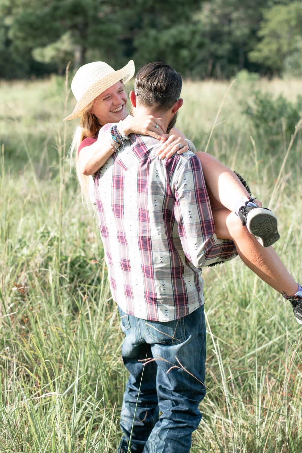 A couple embracing in a sunlit meadow with tall grass and wildflowers.