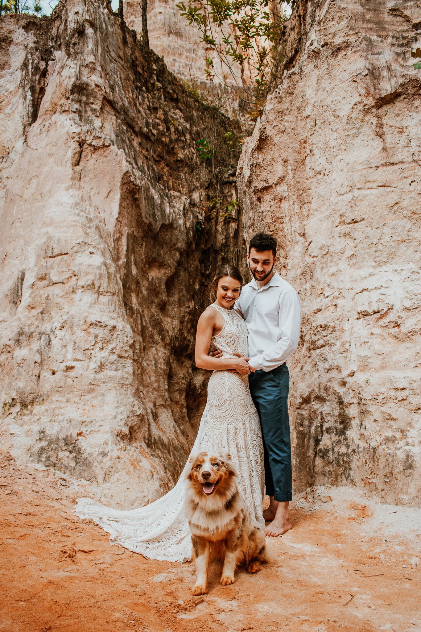 A romantic engagement photoshoot in front of a rocky cliff wall with a fluffy golden dog joining the couple.