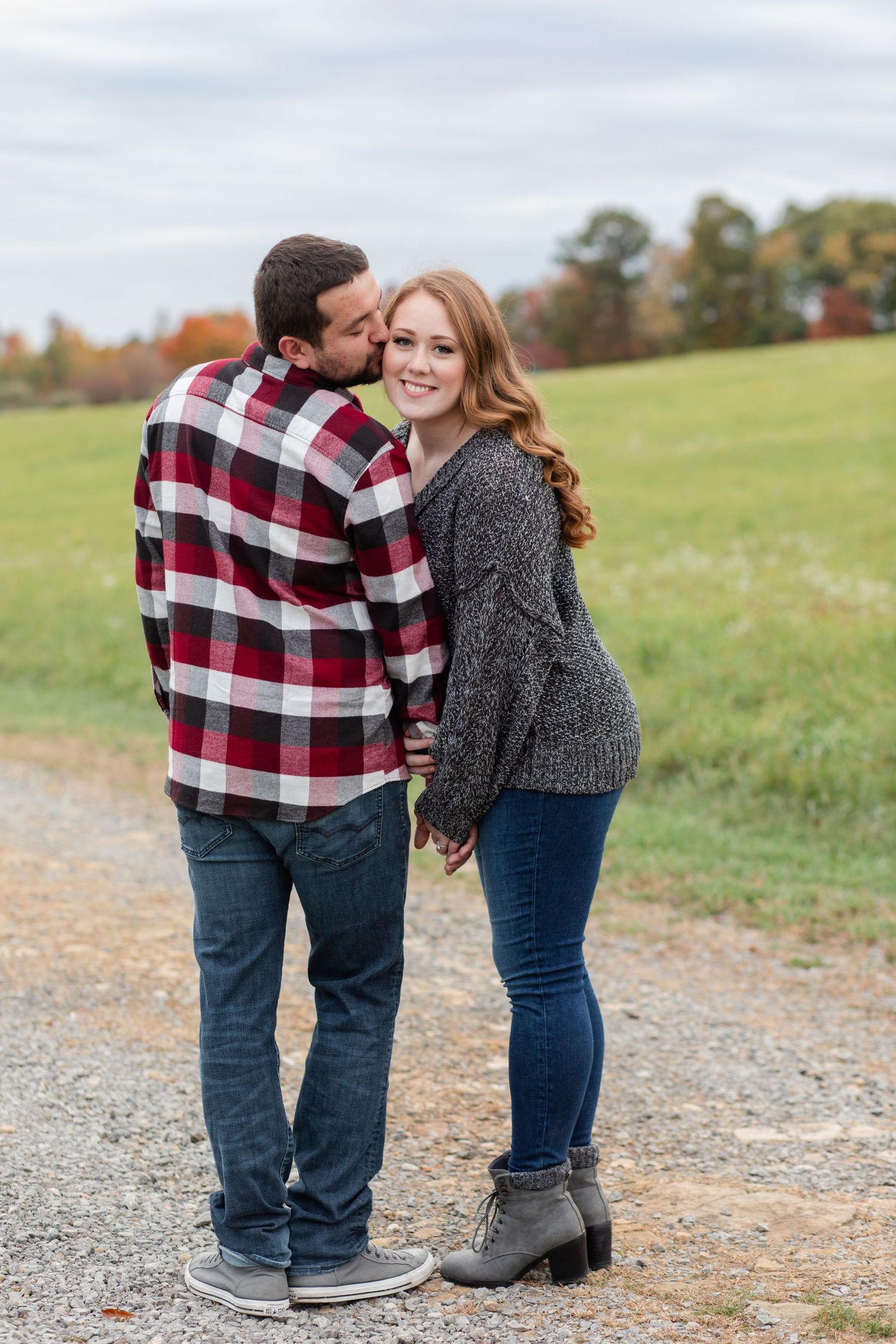 A couple shares an intimate moment on a gravel path surrounded by autumn scenery.
