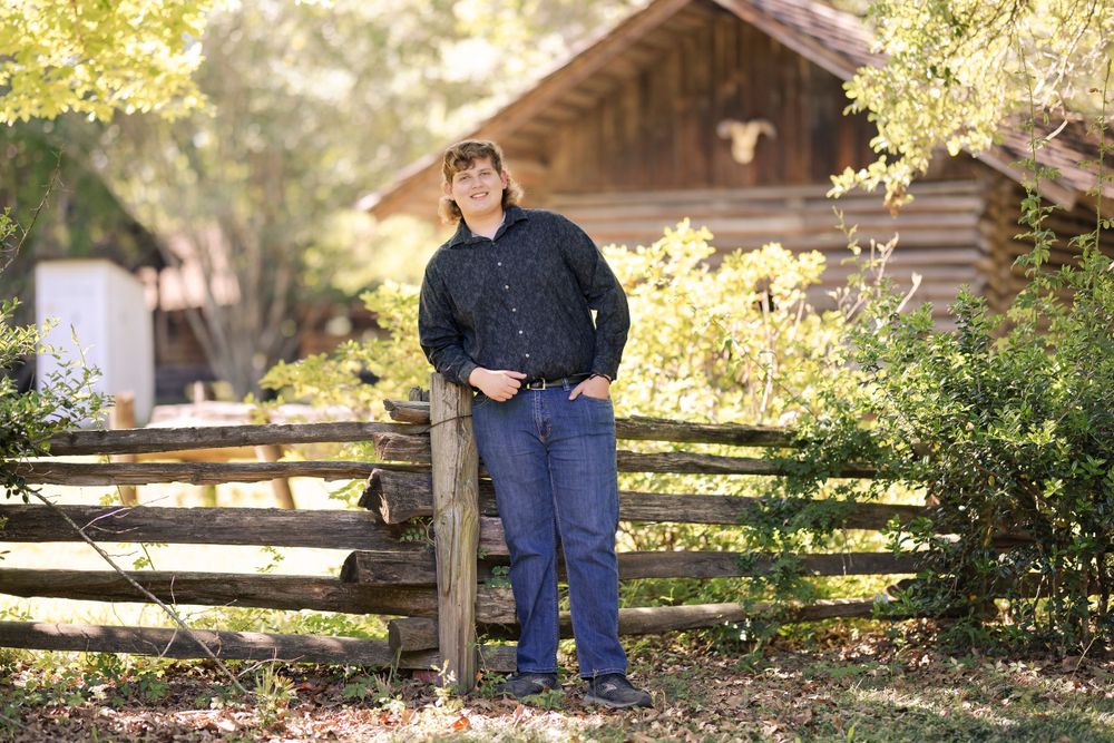 Person in navy shirt leaning on wooden fence with rustic cabin in background.