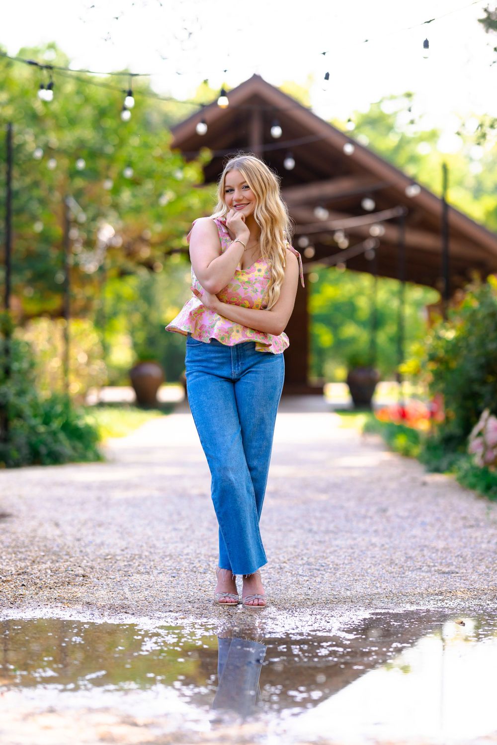 Person in jeans and pink top standing barefoot in puddle on garden path.