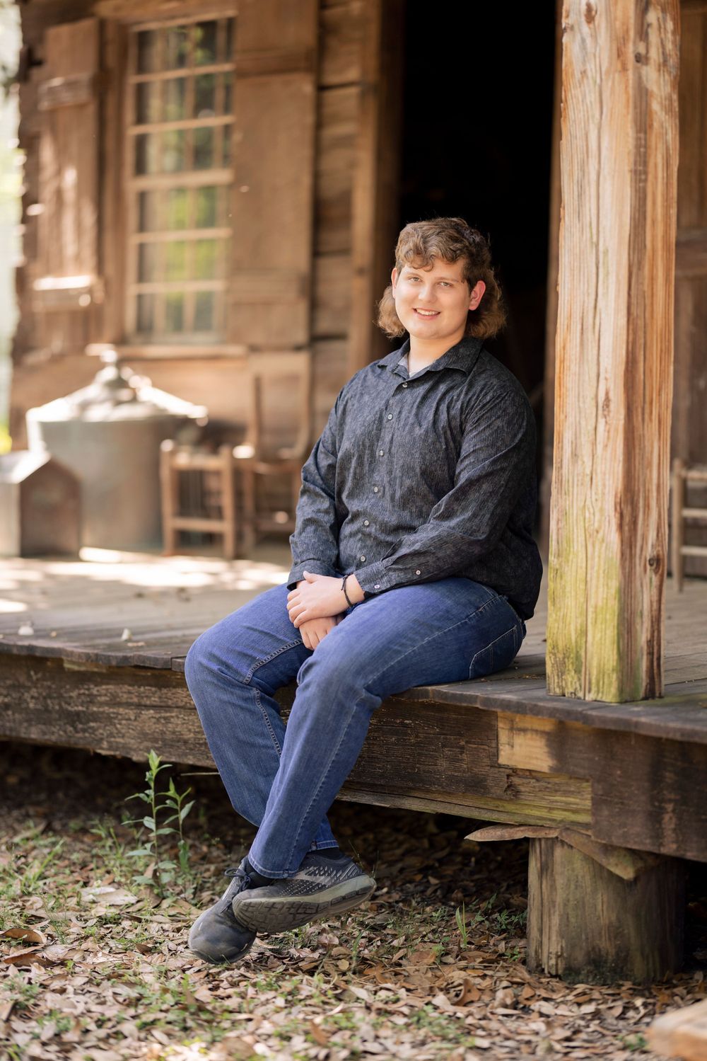 A person in a navy jacket sits casually on the wooden porch of a rustic cabin.