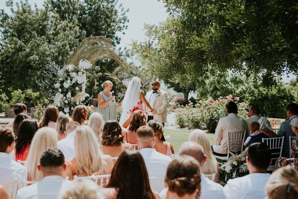 Wedding guests watch ceremony under trees with white floral decorations and mountain views.