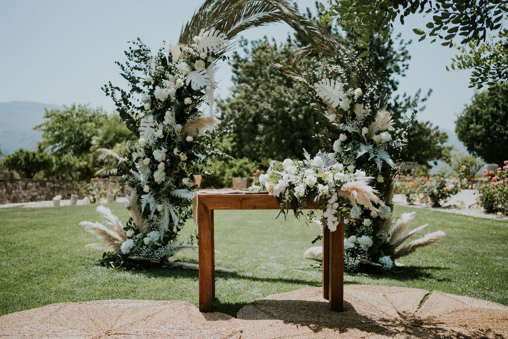 Elegant wooden wedding arch decorated with white flowers and greenery against a mountain backdrop.