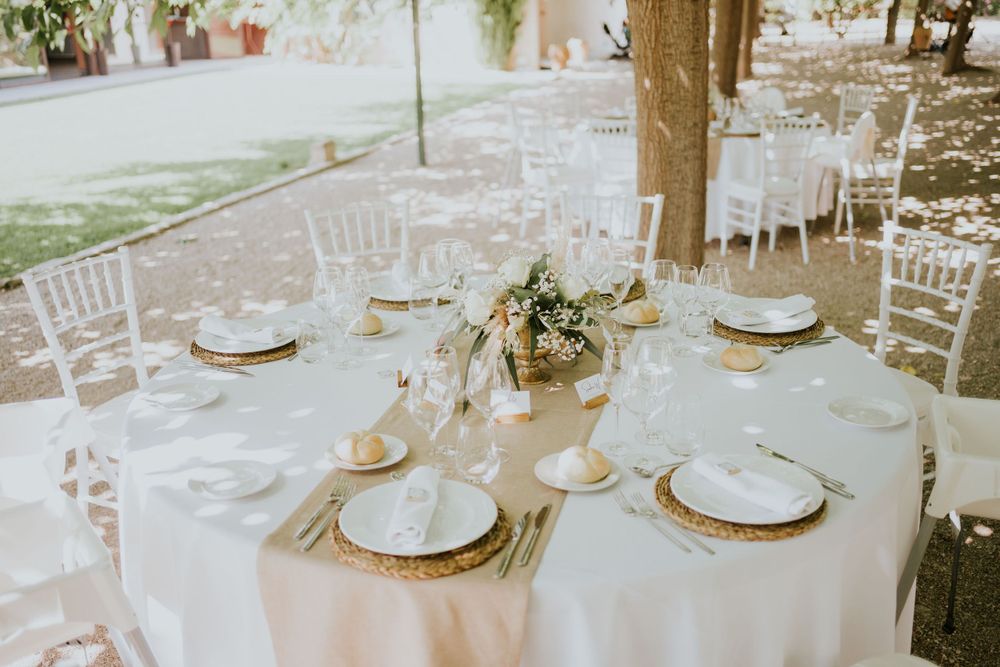 Garden reception tables set with white linens and gold charger plates under trees.