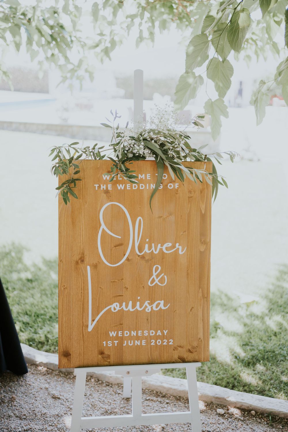 Rustic wooden wedding welcome sign with floral decor displaying names Oliver & Louisa.