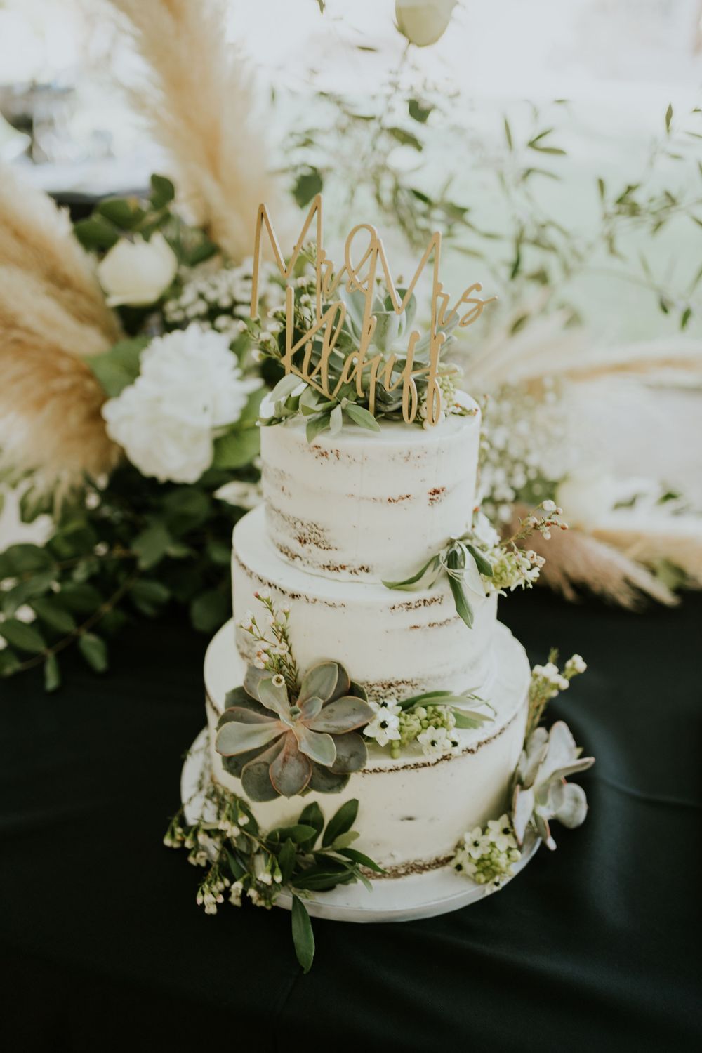 Semi-naked wedding cake decorated with succulents, pampas grass and golden crown topper.