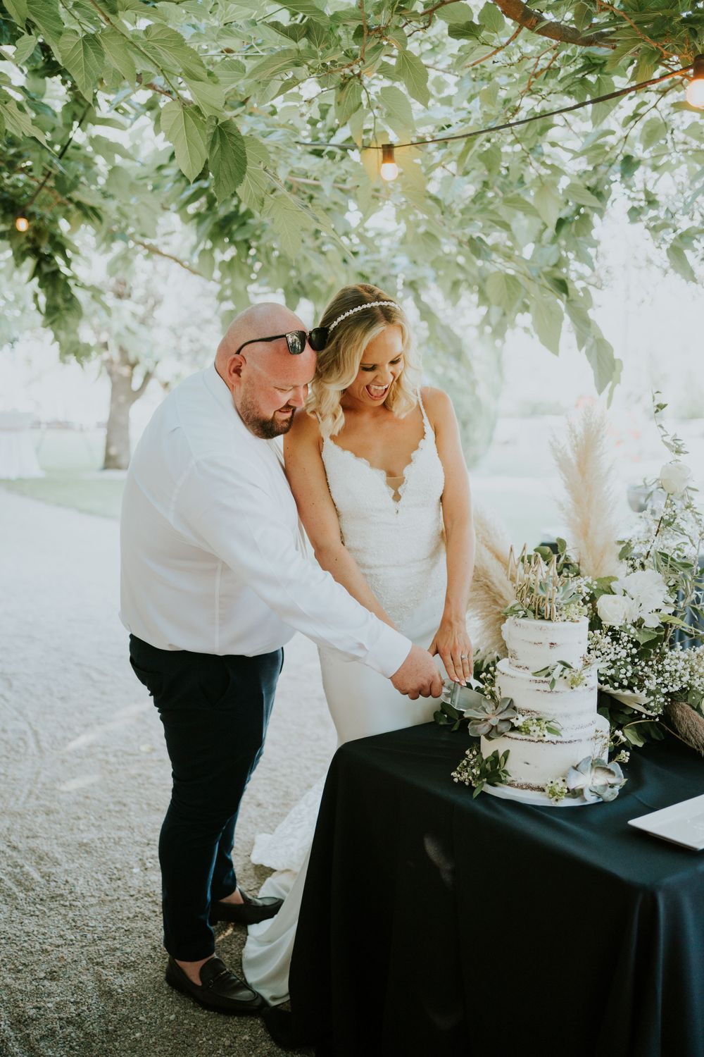 Couple cutting their white wedding cake together at outdoor reception.