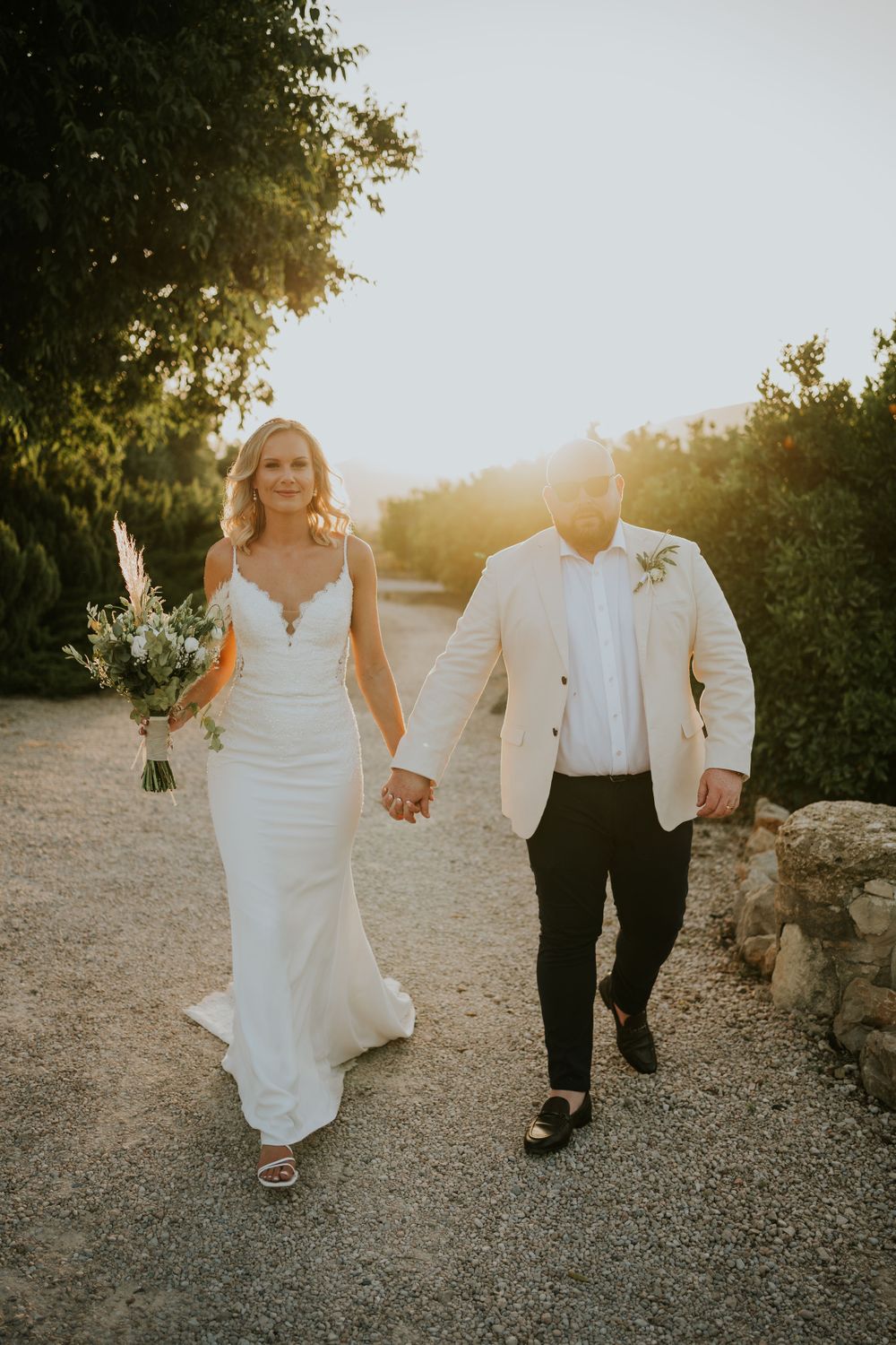 Couple walking hand in hand on garden path during golden hour wedding photos.