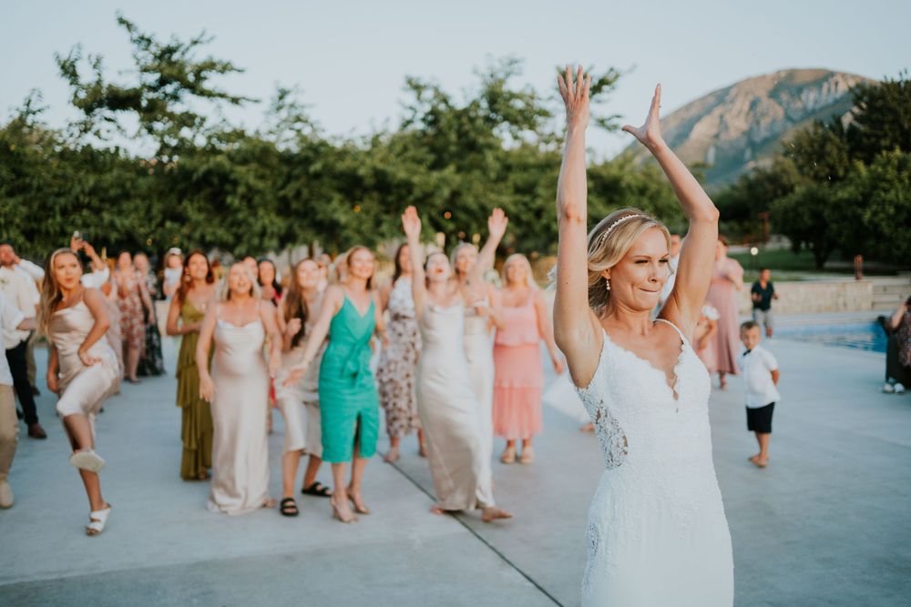 Wedding guests and a bride celebrate with raised arms on an outdoor patio.