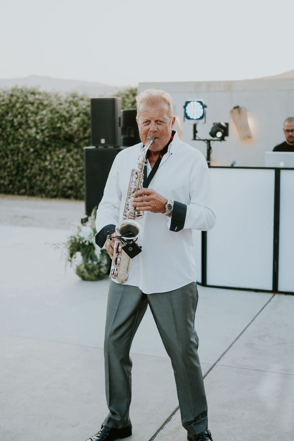 A saxophone player performs in white attire at an outdoor event.