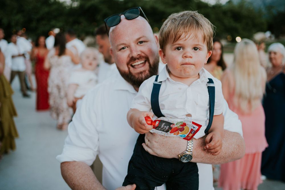 A candid festival moment shared between a bearded adult and small child in suspenders holding candy.