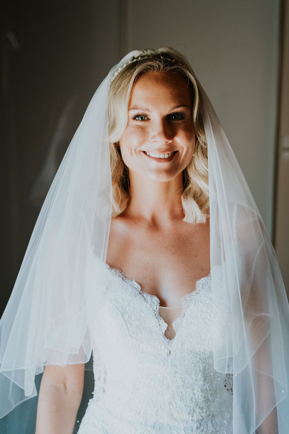 Bridal portrait showing delicate lace wedding dress and flowing veil in natural light.