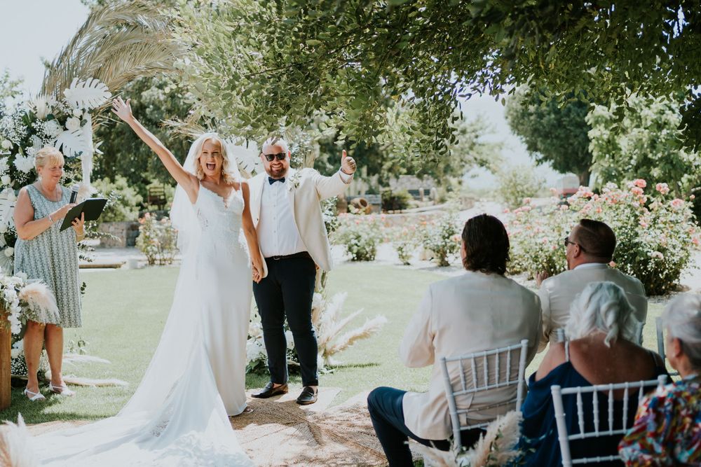 Newlyweds celebrate with raised arms during recessional as guests cheer.