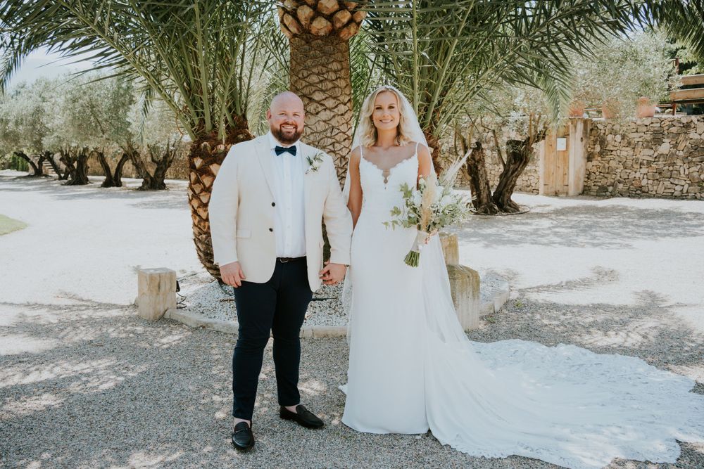Couple poses together against palm trees in wedding attire on their special day.