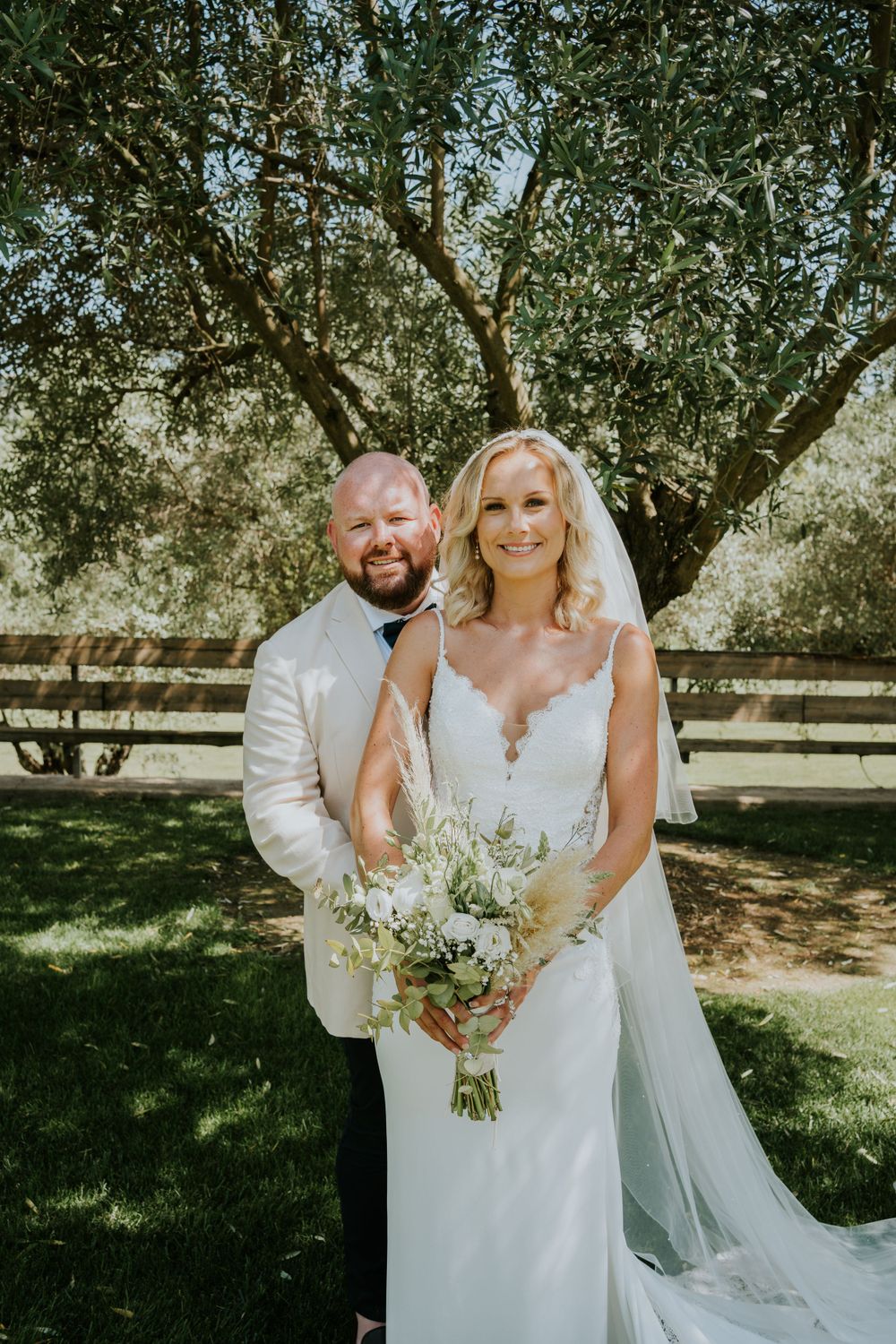 Couple poses under shaded tree during outdoor wedding photoshoot.