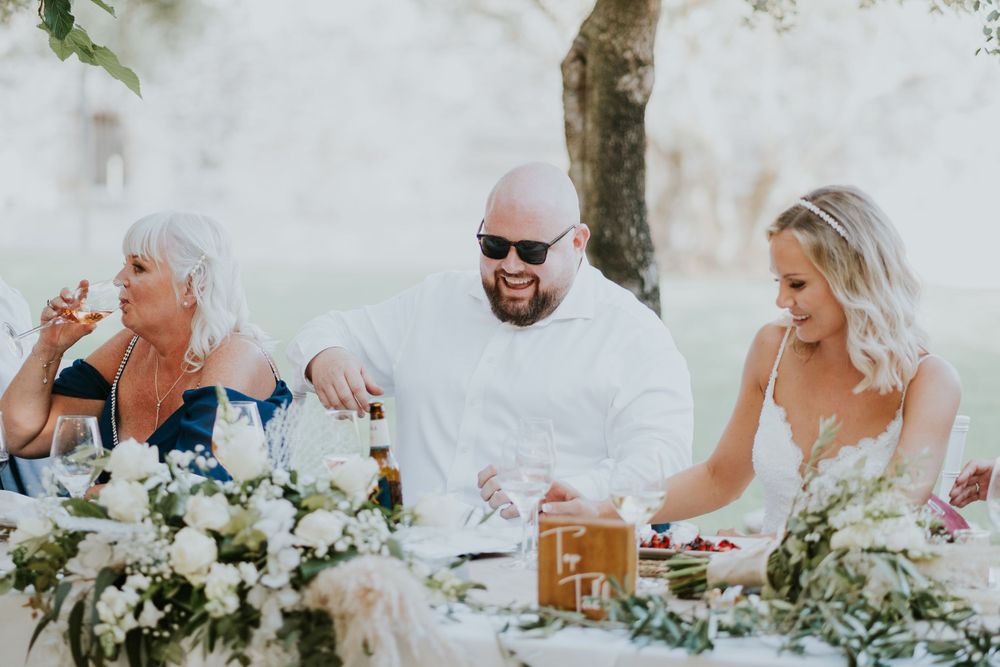 Wedding guests enjoy a sunny outdoor reception dinner with white floral centerpieces and table decor.
