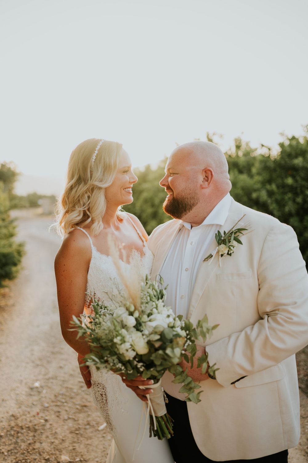 A romantic sunset wedding portrait captures a couple in white attire with a bridal bouquet.